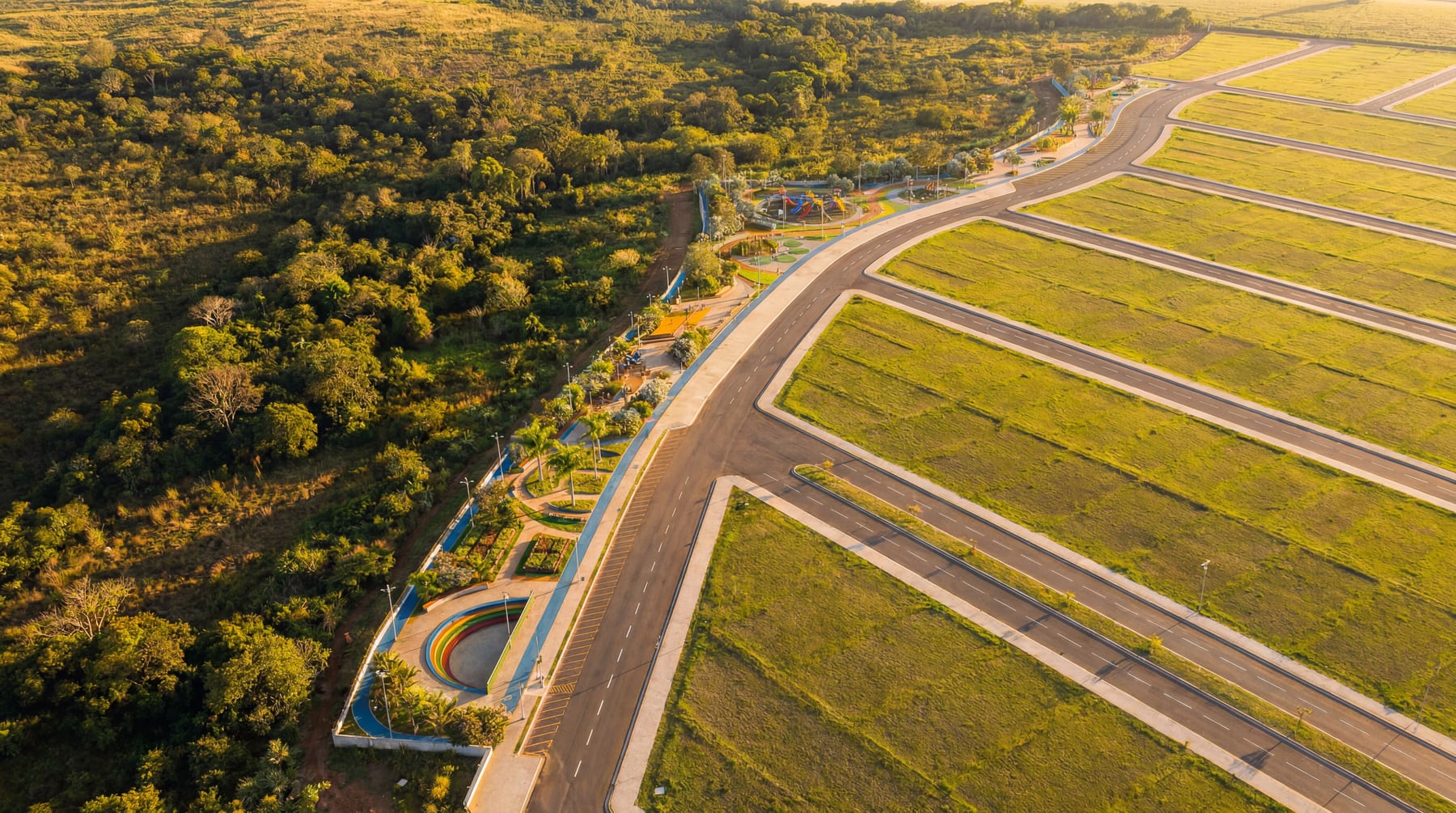 Render aéreo ao entardecer com a mata à esquerda, o parque linear e as quadras de lotes à direita