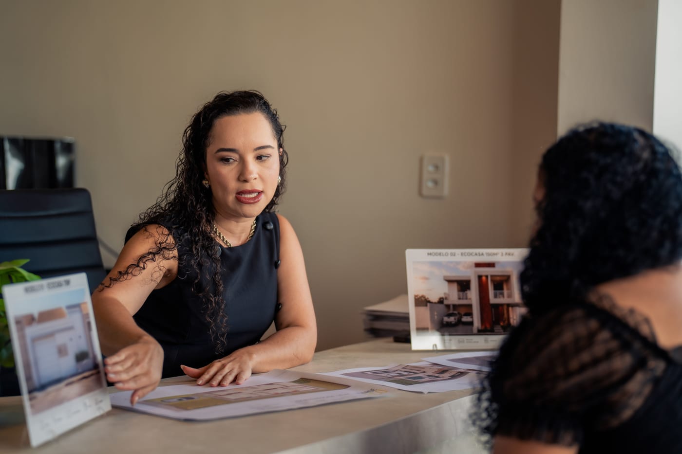 Foto de uma consultora da Eco apresentando plantas de casas a uma visitante na mesa de atendimento